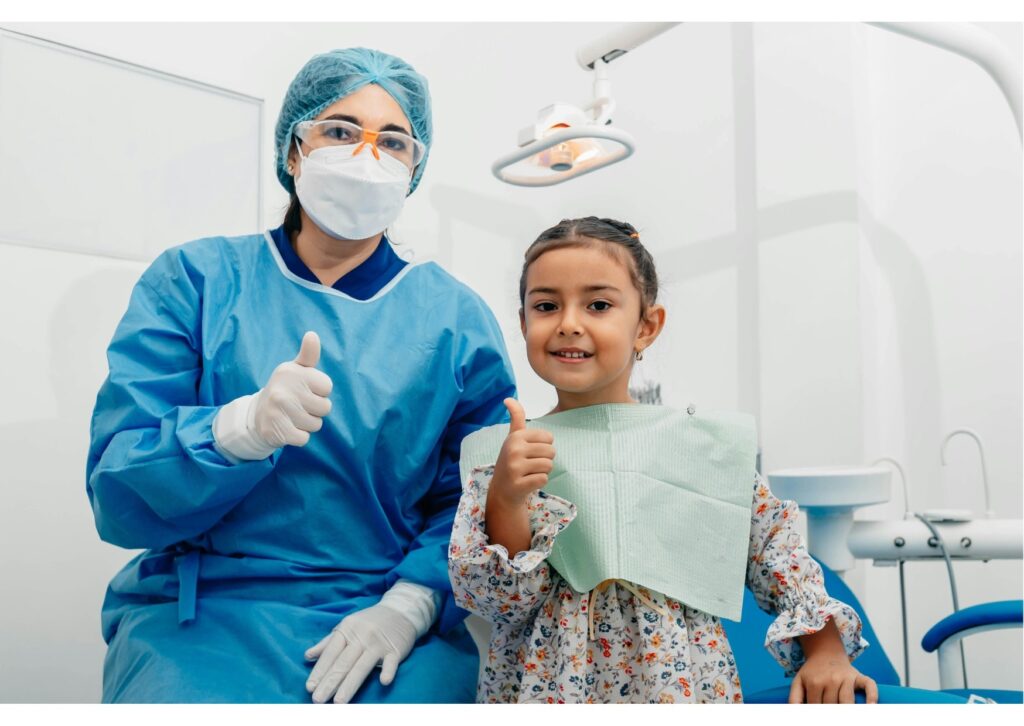 Young child smiling beside a pediatric dentist during a positive children’s dental visit